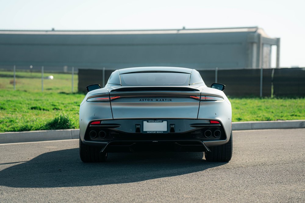 Wide straight rear view of the matte-finish Aston Martin DBS beside a grassy roadside