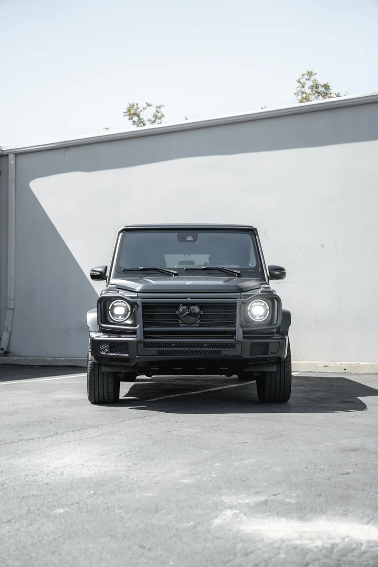 Tall complete straight front portrait of the G 550 below a diagonal wall shadow, with its circular headlamps visible