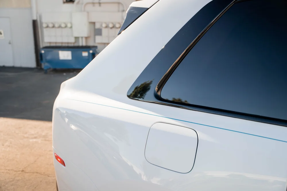 White Rolls-Royce Cullinan — rear-quarter glass, fuel door and thin turquoise side coachline