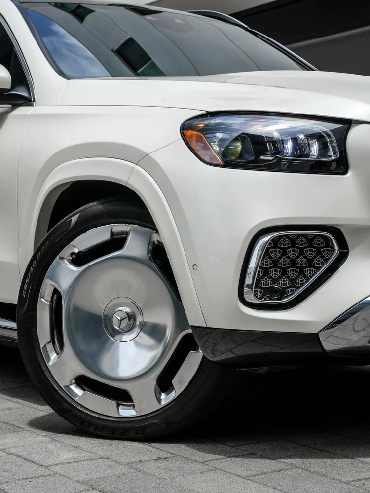 Close view of the polished front wheel, white fender, headlamp and patterned lower grille trim.