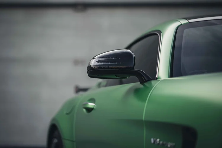 Dark mirror above the green door and fender, with the side window and silver lettering in a wide shallow-focus view.