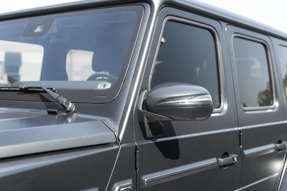 Grey G 63 side glass and dark mirror beside the windshield, black window frames and exposed door hinge