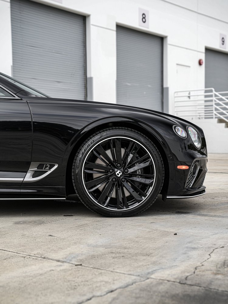 Bentley Continental GTC front wheel and black fender in side view, with the side vent and lower chrome trim visible.