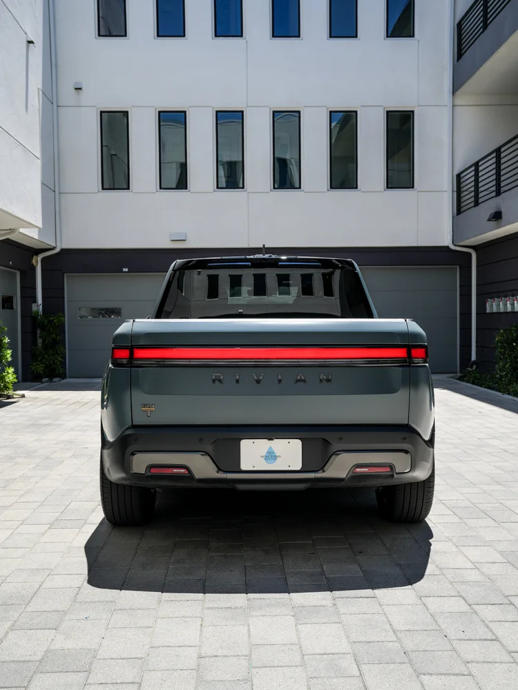 Centered rear view of the Rivian R1T showing its satin tailgate, red light bar, rear glass, Toyz plate, rear wheels and bumper.