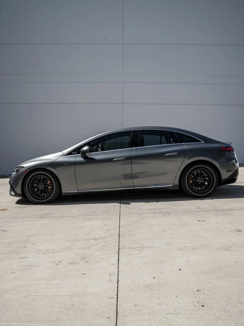 Full side profile of the gray Mercedes-AMG EQE 53 with black multi-spoke wheels and reflective side glass.