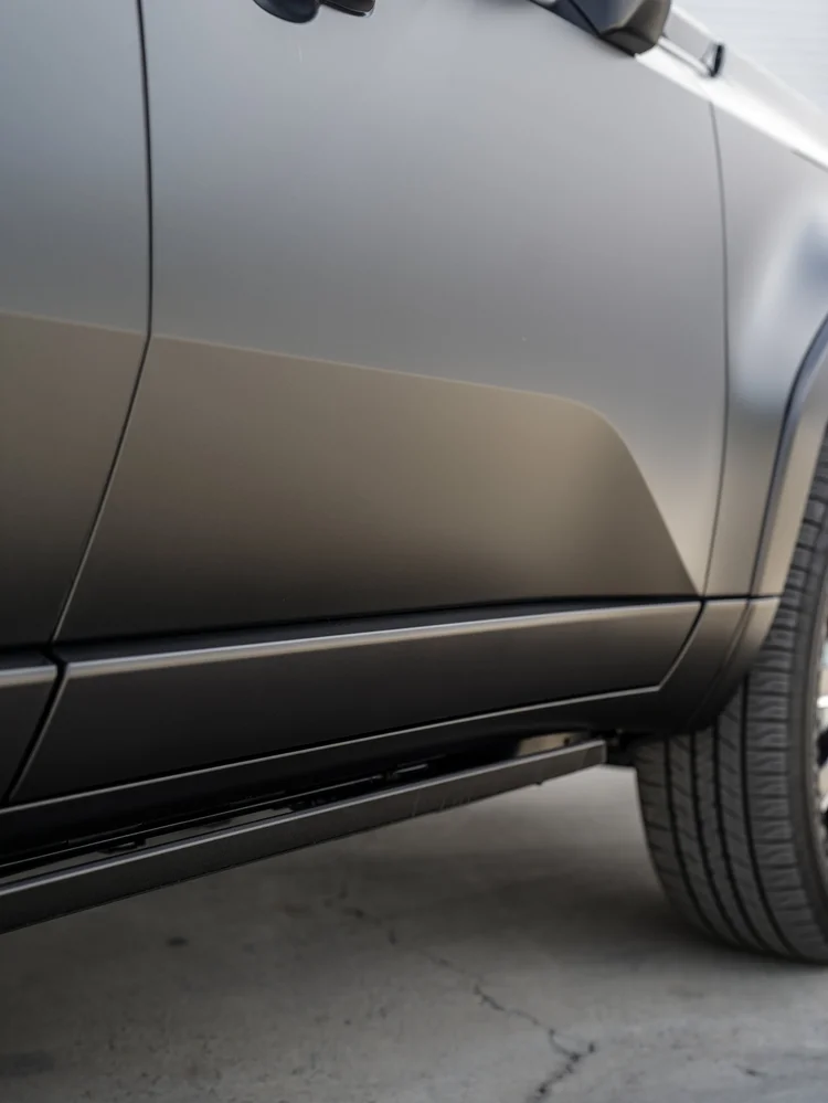 Low door and front-fender detail with soft highlights across dark bodywork, a running board below and part of the front tire at right