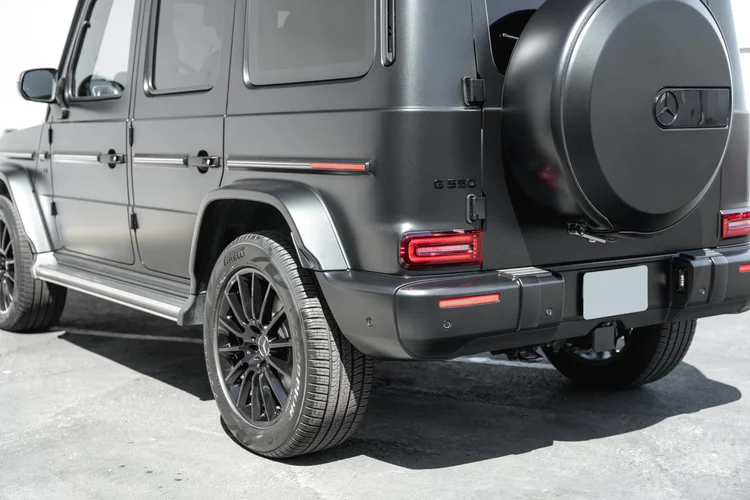Close rear-side view of the grey G 550 with a black wheel, round spare-wheel cover, silver running board and side doors