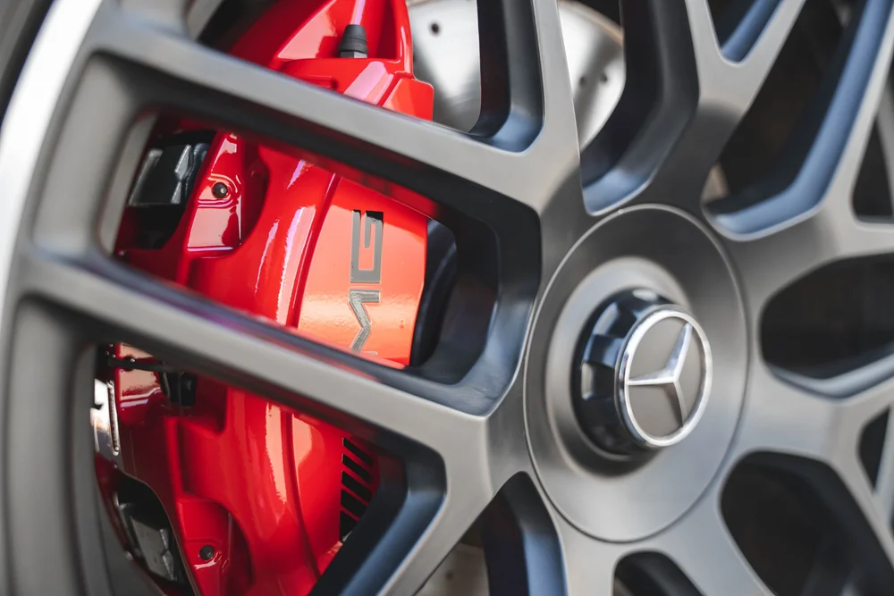 Close view of a red AMG-lettered caliper behind dark wheel spokes beside a Mercedes-star wheel center