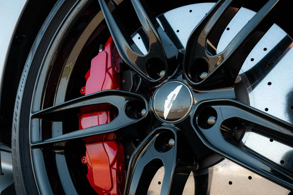 Black DBS wheel with a red brake caliper and perforated brake disc behind the spokes