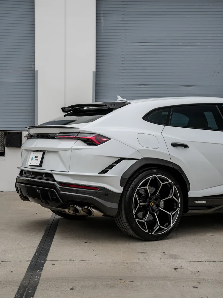Close rear-quarter view of the white Urus with its roof spoiler, red rear lamp, rear wheel, lower trim and exhaust outlets.