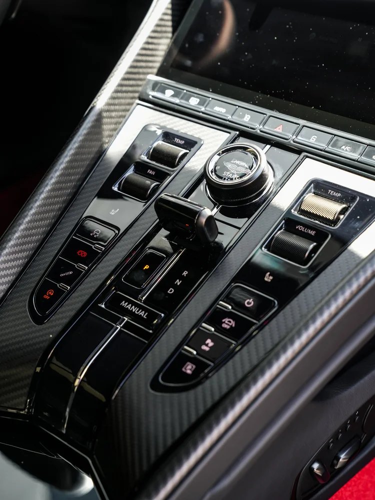 DB12 center-console controls and selector surrounded by dark weave-pattern trim.