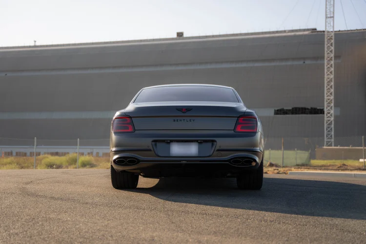Complete low rear view of the gray Bentley with a wide building in the background.