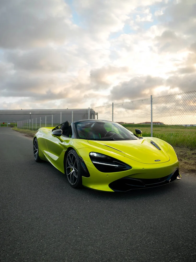 Bright green McLaren 720S in a complete front-three-quarter view outdoors beside a fence