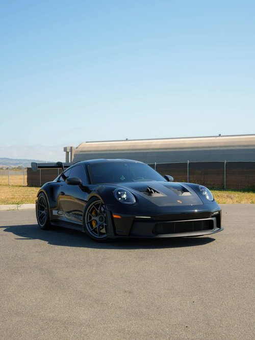 Black Porsche GT3 RS in a front three-quarter view with grey wheels, yellow brake calipers and a large rear wing outdoors