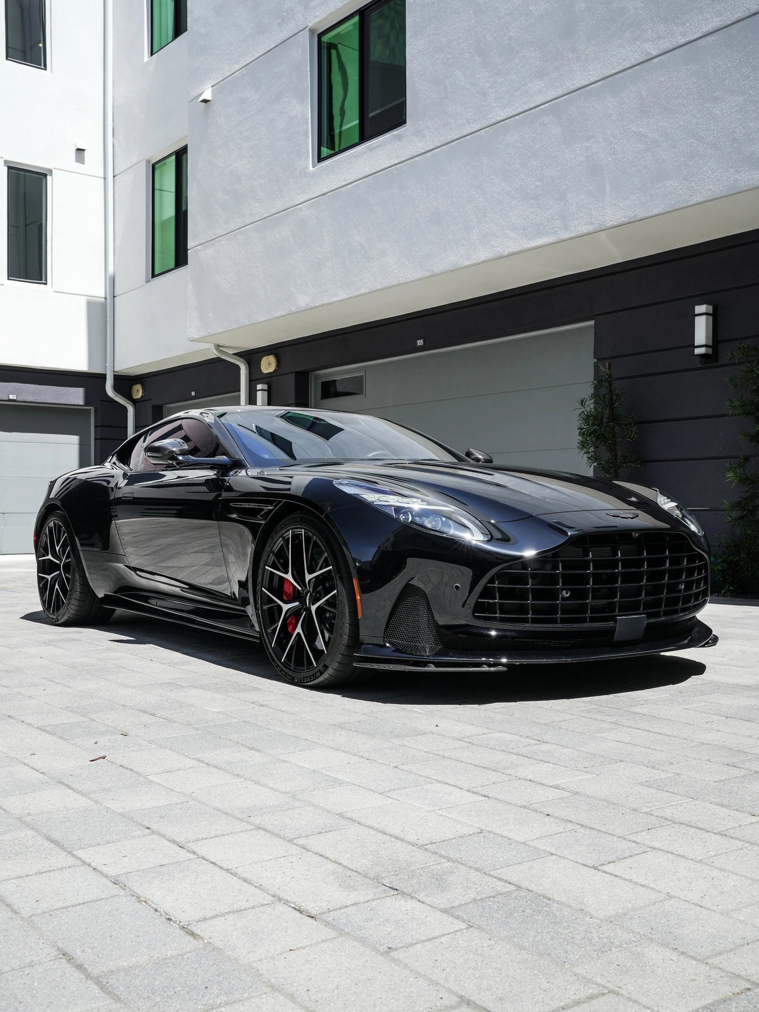 Black Aston Martin DB12 in a front three-quarter view with its grille, wheels and red brake calipers visible.