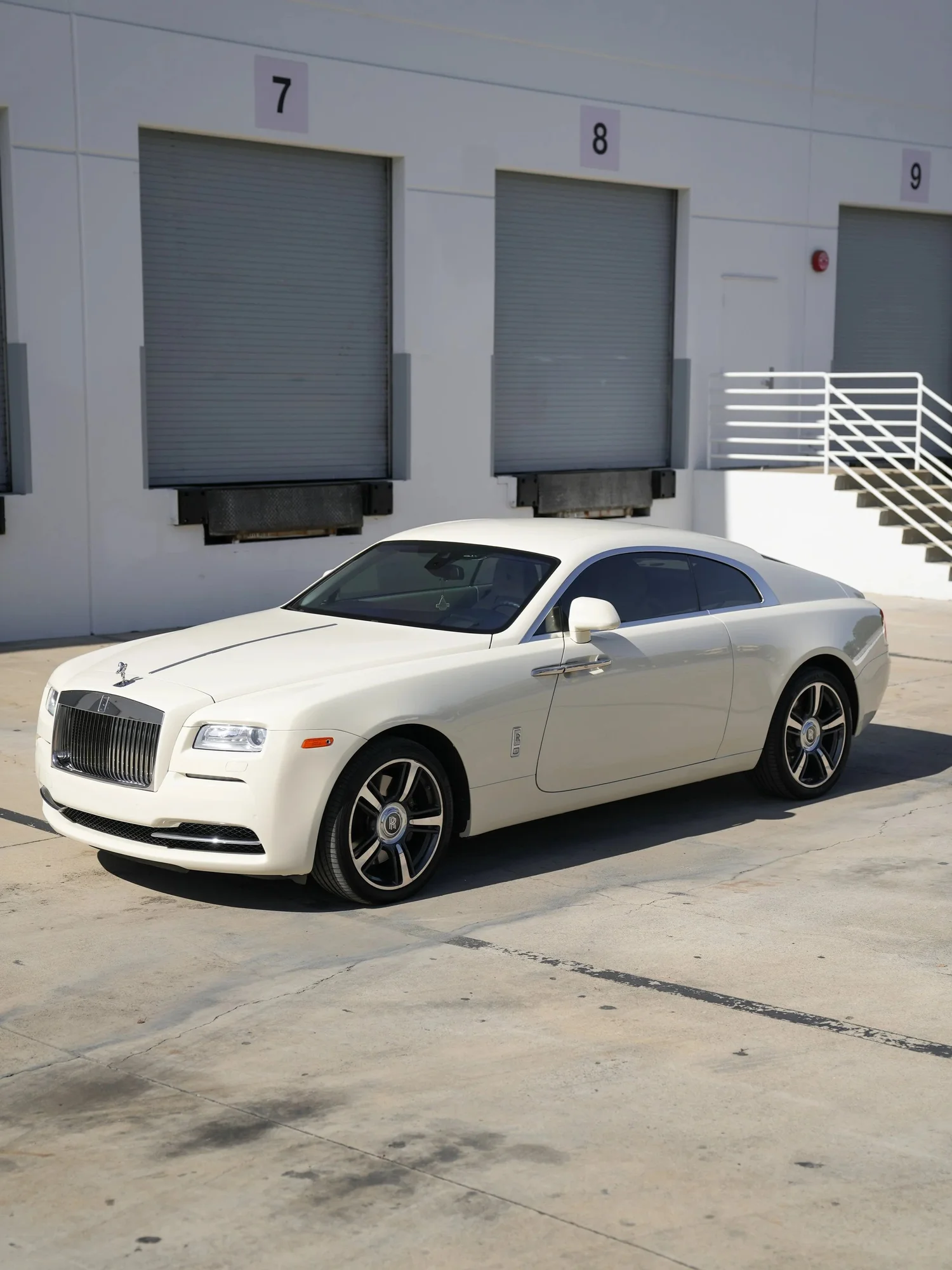 Pale Rolls-Royce Wraith in a complete front three-quarter view beside numbered loading doors.