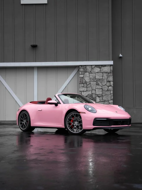 Pink Porsche 911 convertible with red seats, dark wheels and red brake calipers in a front three-quarter view on wet pavement