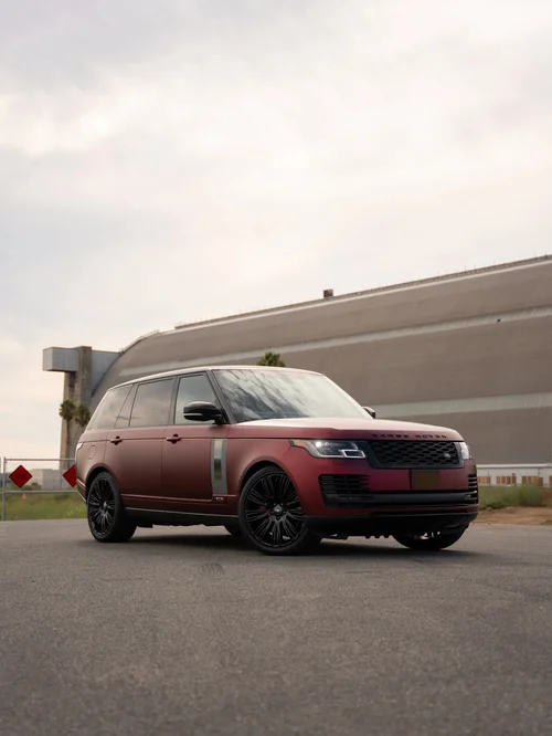 Dark red Range Rover in a front three-quarter view outside an industrial building.