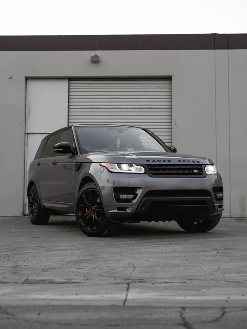Metallic grey Range Rover in a front three-quarter view outside a roll-up garage door, with black wheels and red brake calipers