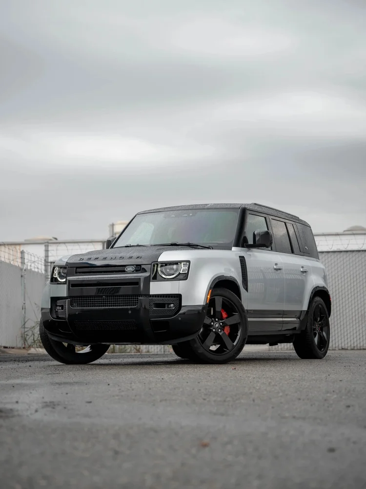 Gray Land Rover Defender in a complete front-three-quarter view with black wheels and red calipers on a paved lot