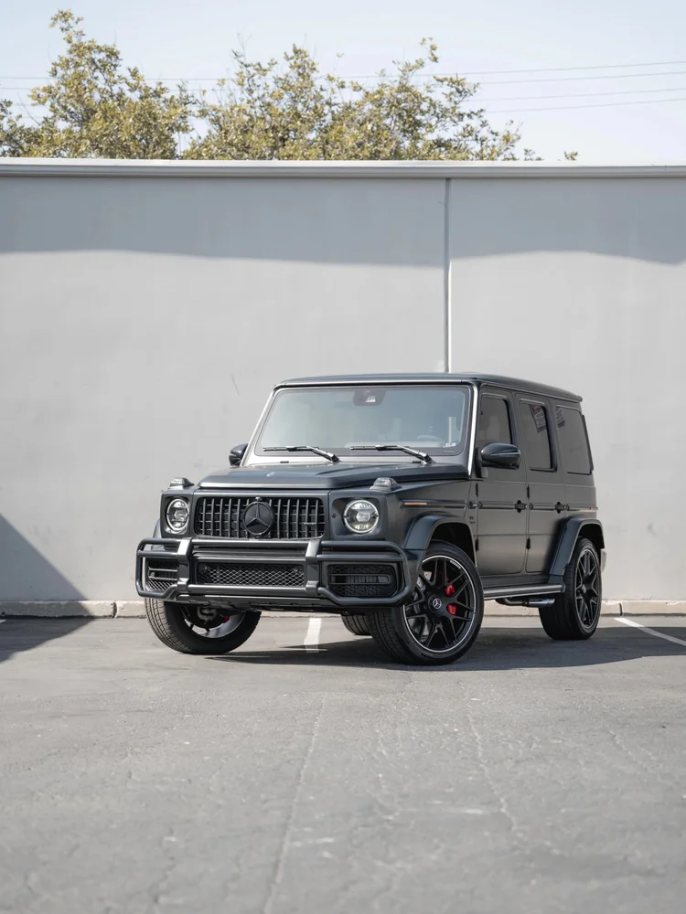 Complete front-three-quarter view of the charcoal-grey Mercedes-AMG G 63 with dark wheels and red calipers in a portrait frame