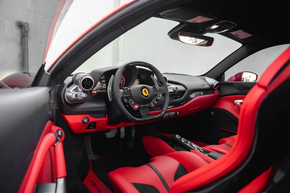Ferrari F8 cockpit with black steering wheel, red seats and dashboard seen through the open driver door