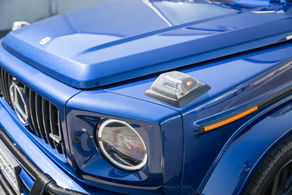 Blue G 63 front-corner detail with a clear fender-top lamp, amber reflector, circular headlamp and reflective hood