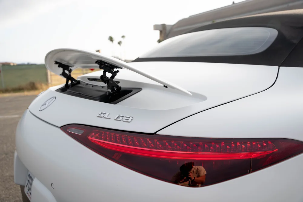 White rear-body detail with a raised spoiler on black supports, SL 63 lettering, a red lamp and rear glass in the dark roof