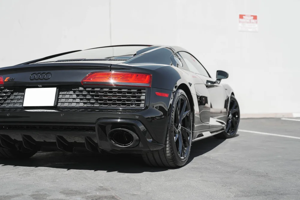 Low rear-quarter view of the black Audi R8 with taillight, rear wheel, large exhaust outlet and diffuser