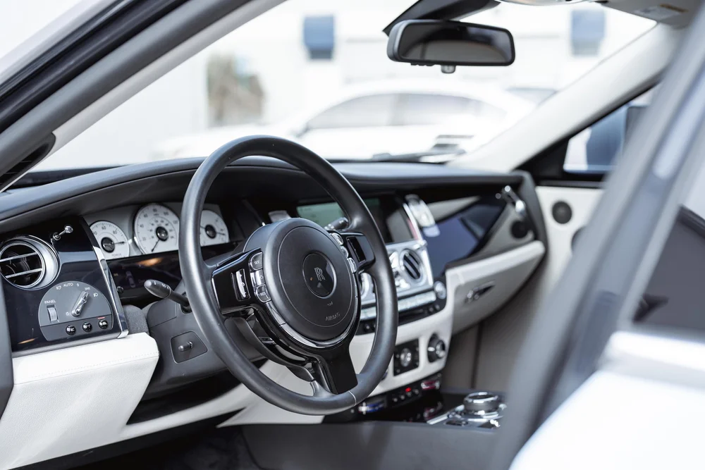 Rolls-Royce Ghost — steering wheel, dashboard and white cabin trim viewed through the open front doorway