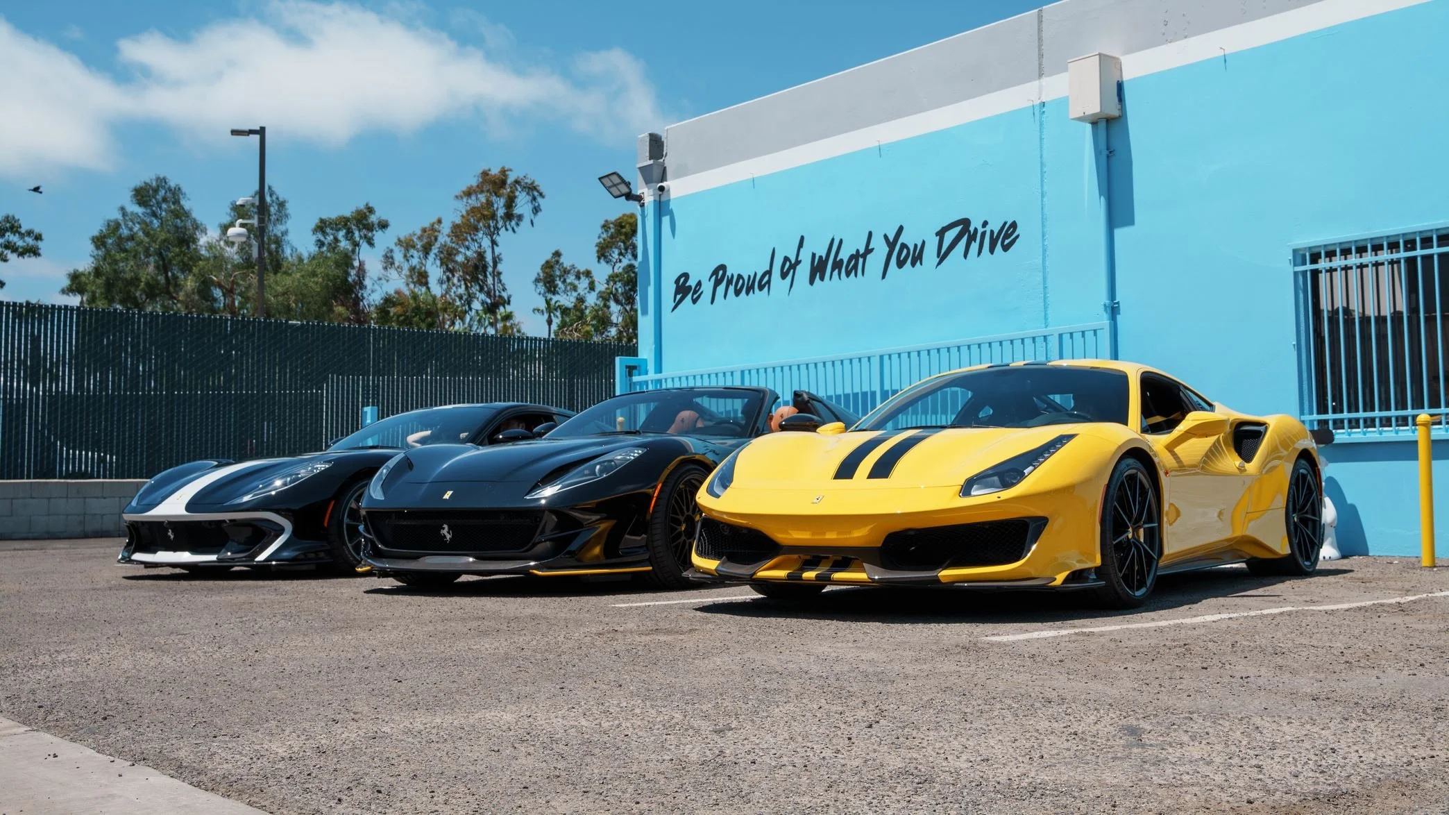 Three Ferrari sports cars parked outside the blue Toyz Detail Studio building in Irvine