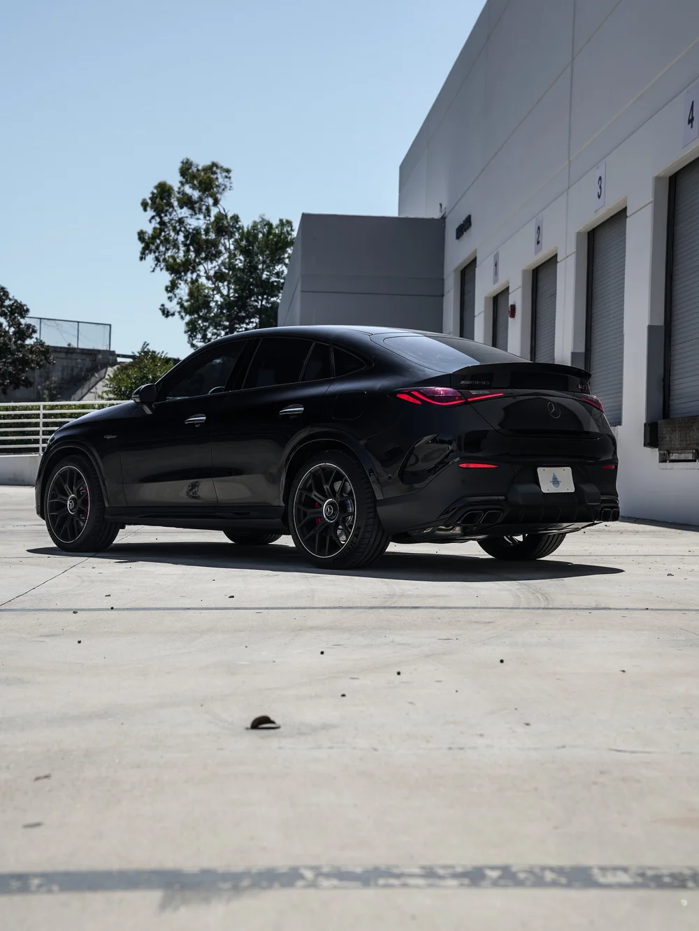 Complete rear three-quarter view of the black Mercedes-AMG GLC 63 S facing left, with a sloping roofline, red taillights, dark wheels and four rectangular exhaust outlets.