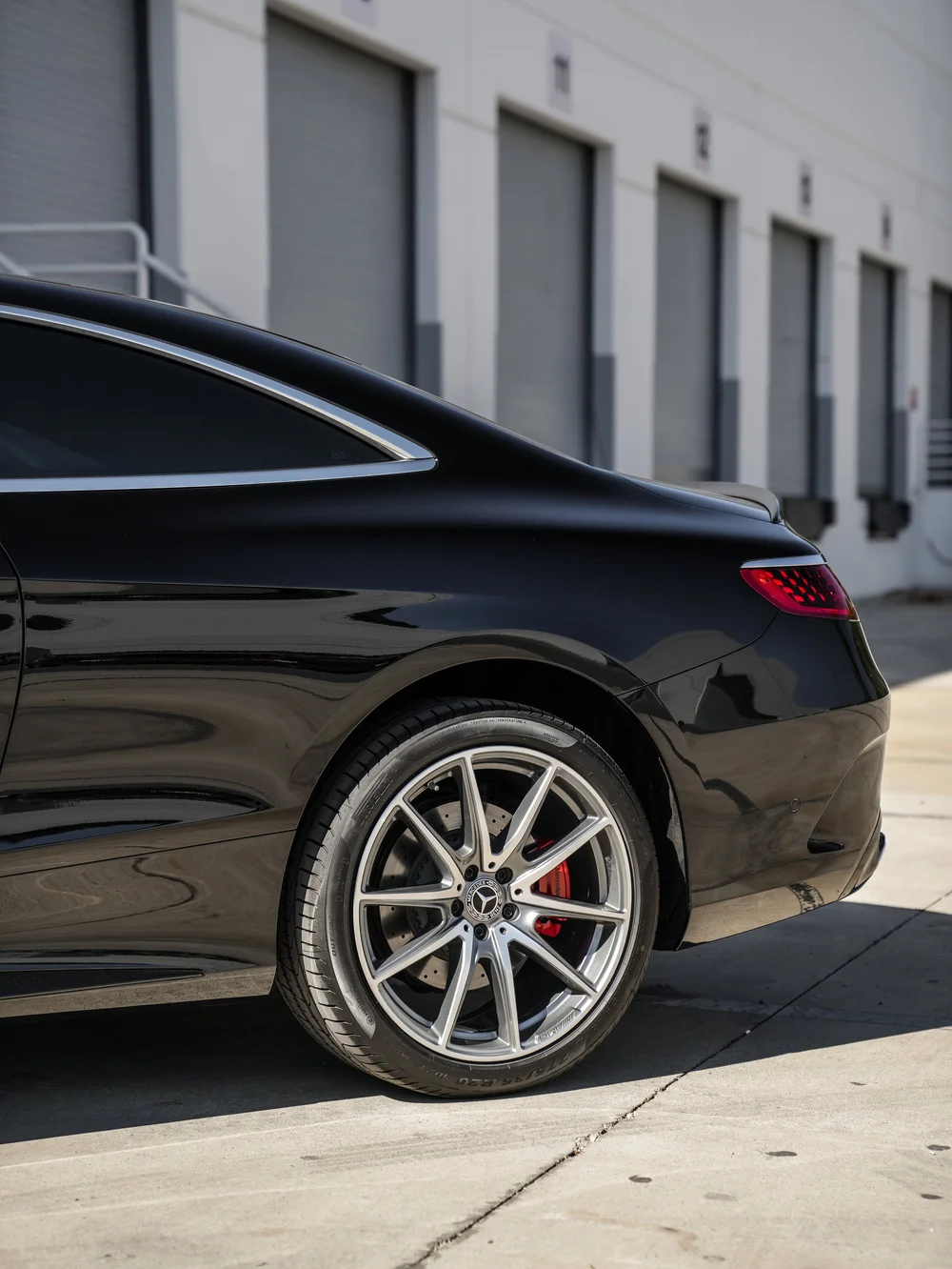 Rear-quarter detail of the black Mercedes-Benz S 560 showing the silver multi-spoke rear wheel, red brake caliper, bright window surround and red taillight.