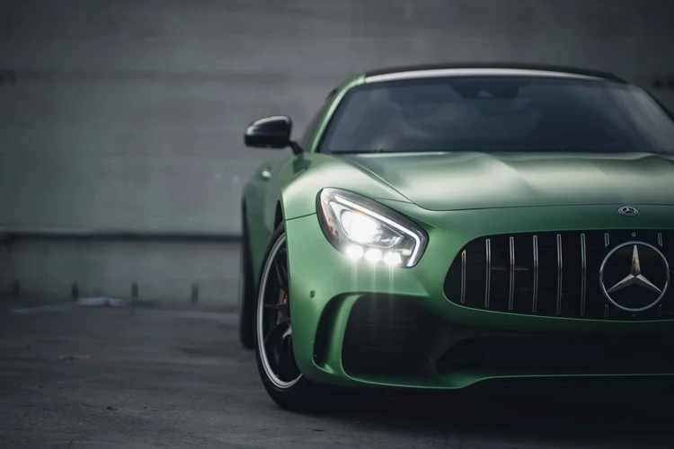 Partial green front corner with an illuminated headlamp, curved hood and vertical grille bars.