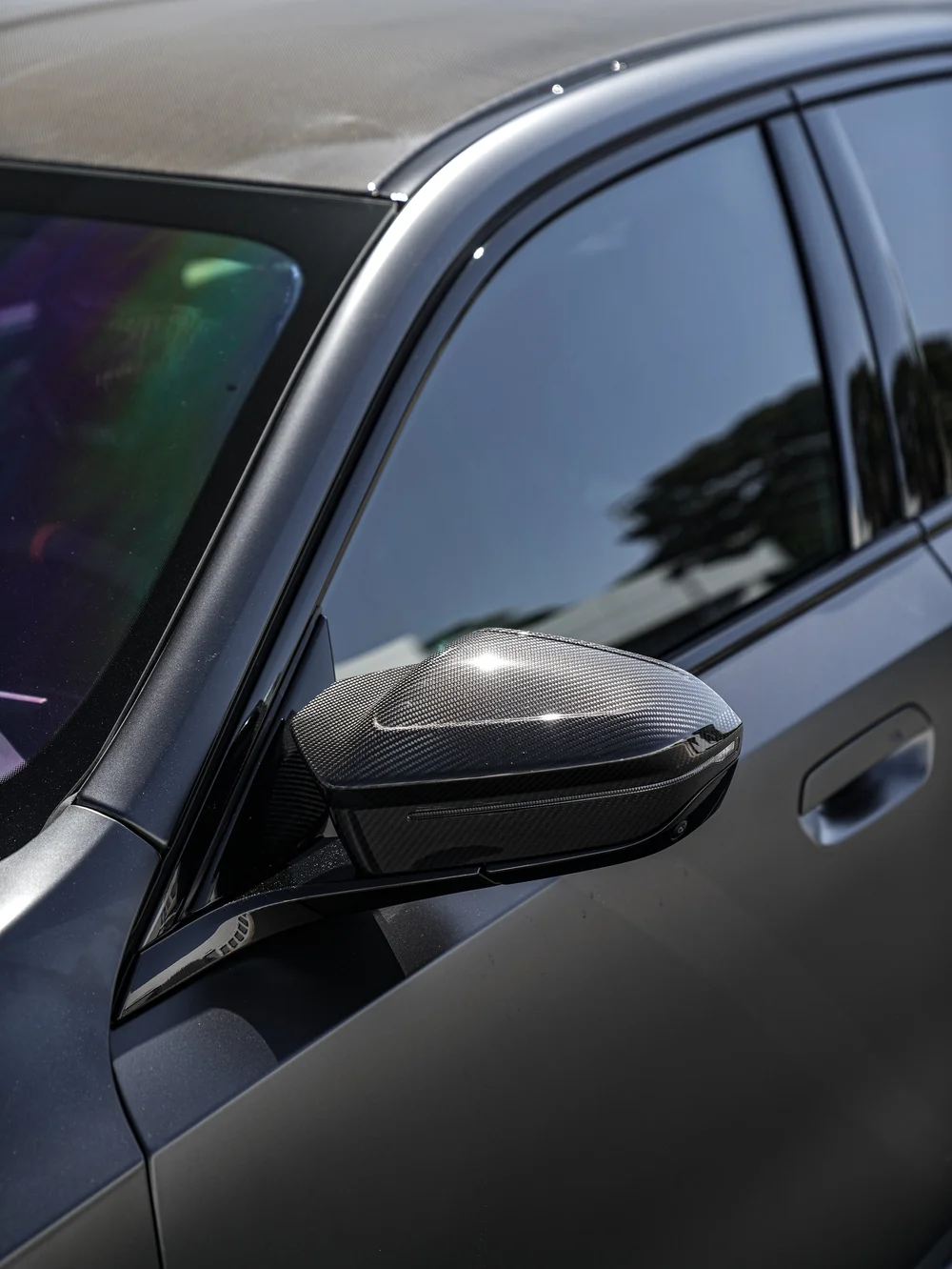 BMW G90 M5 side mirror and dark front side window, with reflections in the glass and matte door below