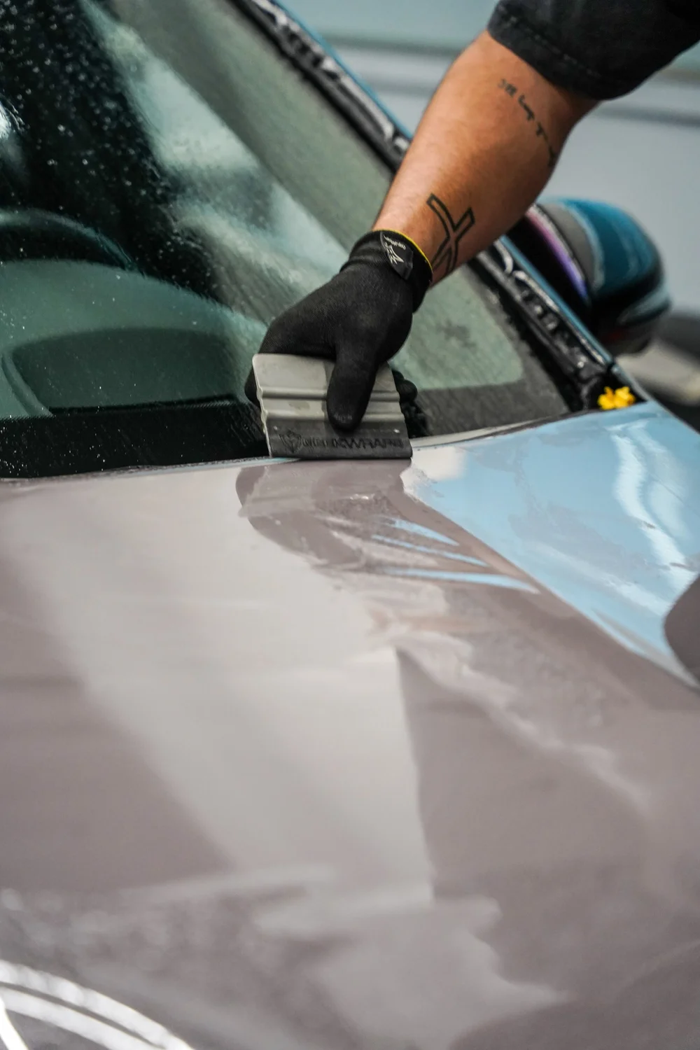 Gloved hand using a squeegee on light-grey vinyl beside the wet windshield