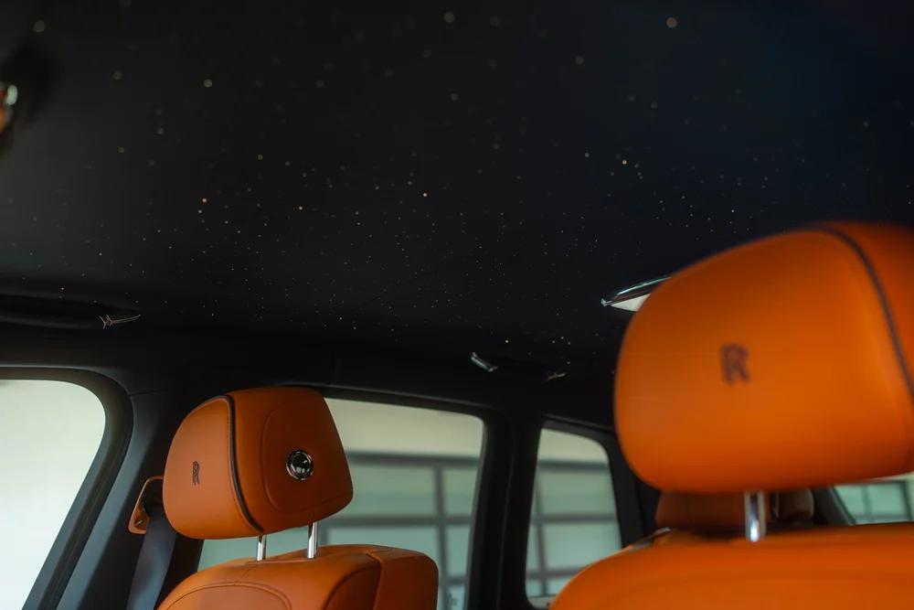 Black Rolls-Royce Cullinan Black Badge with Two-Tone Wheels — orange cabin headrests beneath a dark headliner with small ceiling lights
