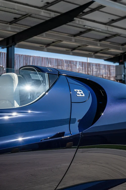 Bugatti W16 Mistral opposite Blue Carbon side panel and EB emblem below the cockpit edge in sunlight
