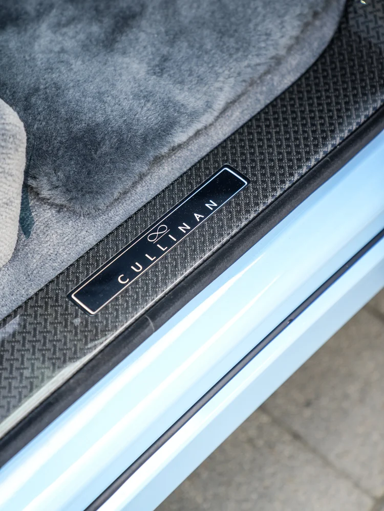 CULLINAN lettering and infinity emblem on the dark patterned door sill beside pale carpet and Powder Blue bodywork
