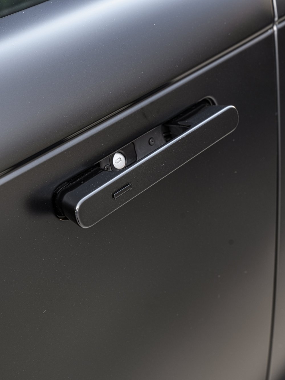 Close-up of an extended black door handle and the surrounding satin-looking panel.