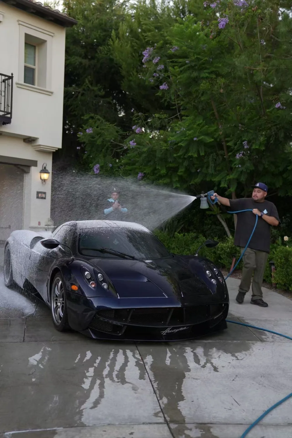 Toyz detailer pressure-washing a black sports car at a home