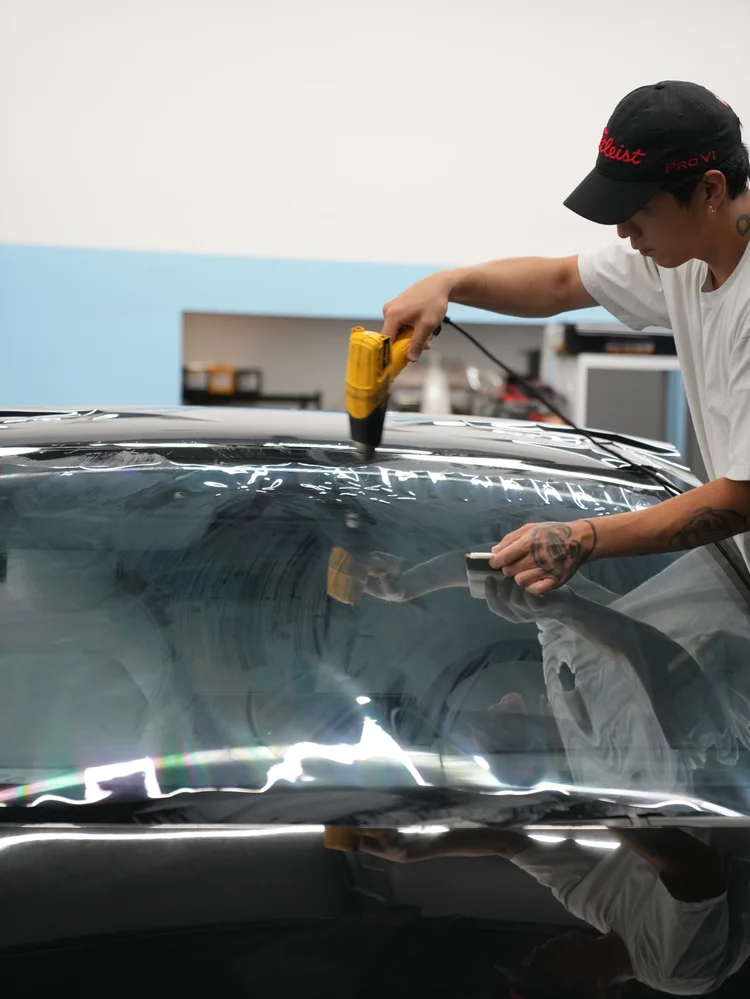 Installer using a yellow heat tool and white squeegee over a wet front windshield sheet in the original project gallery