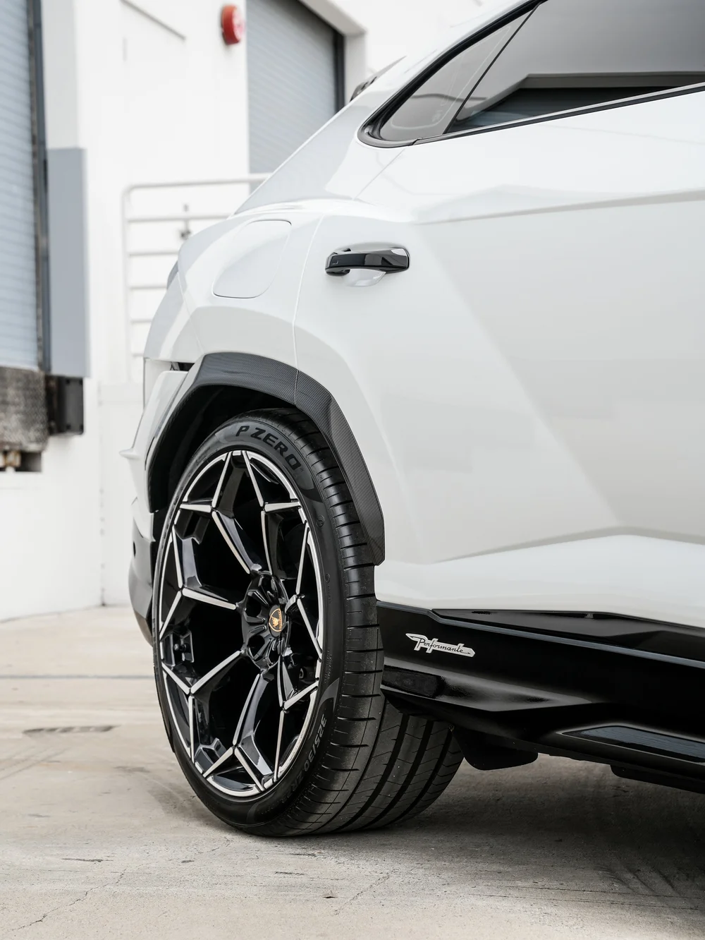 Rear wheel beside the white rear door and quarter panel, woven-pattern arch trim, dark side glass and Performante sill lettering.