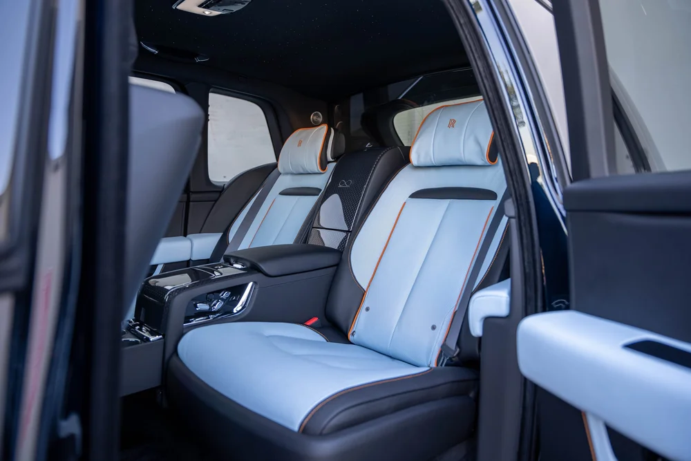 Black Rolls-Royce Cullinan Black Badge — pale rear seats with orange piping and the cabin center console through the open doorway