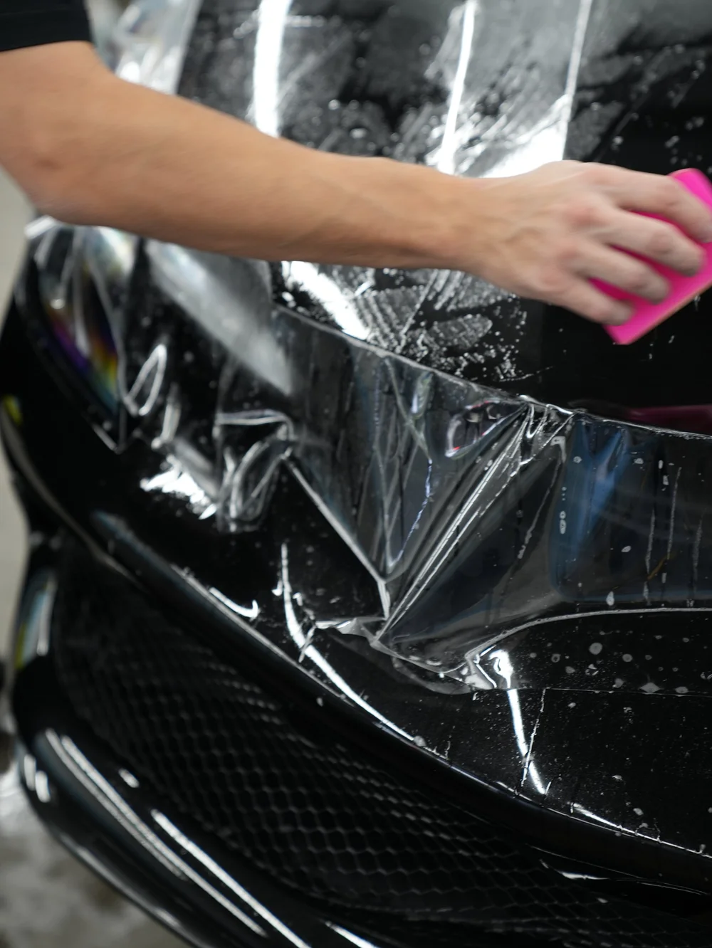 Close view of clear film and a pink squeegee on the Ferrari 296 GTB front bodywork