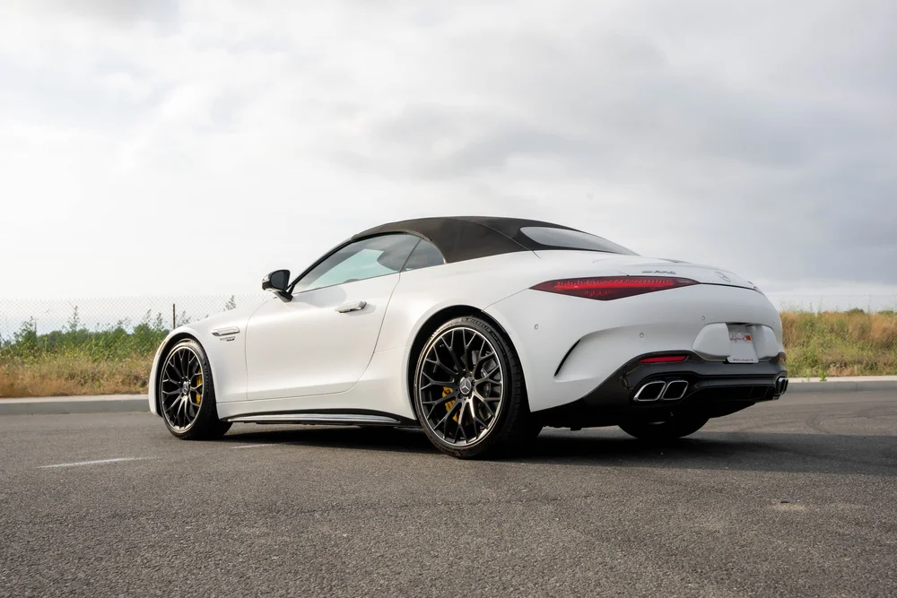 Complete low opposite rear-three-quarter view of the white SL 63 with dark multispoke wheels, yellow calipers and a dark fabric roof