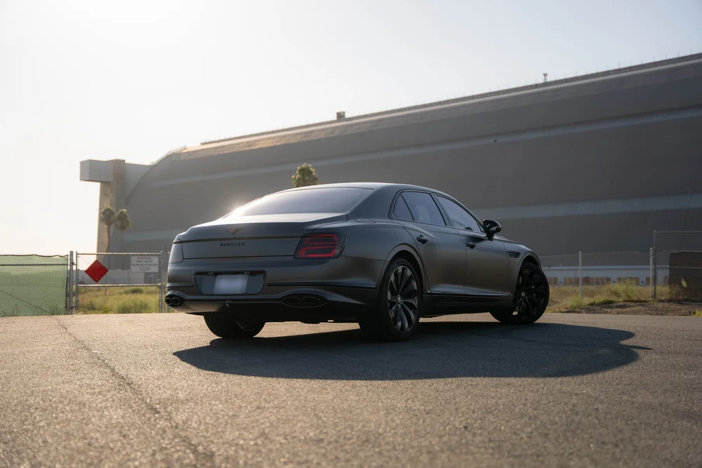 Complete rear-corner view of the gray sedan with sunlight catching the roof and trunk.