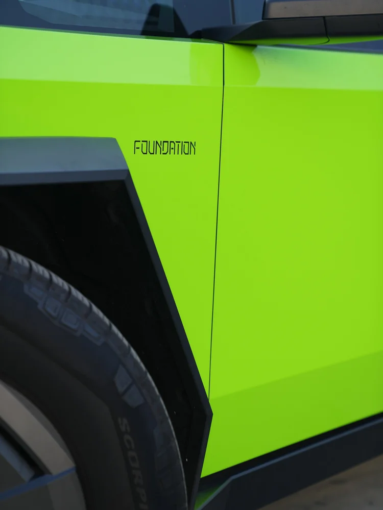Finished green Cybertruck side detail with FOUNDATION lettering beside dark wheel-arch trim, the mirror and a door seam.
