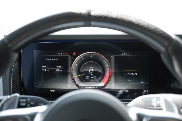 Instrument display viewed behind the G 63 steering wheel, with digital gauges and red-and-black cabin trim