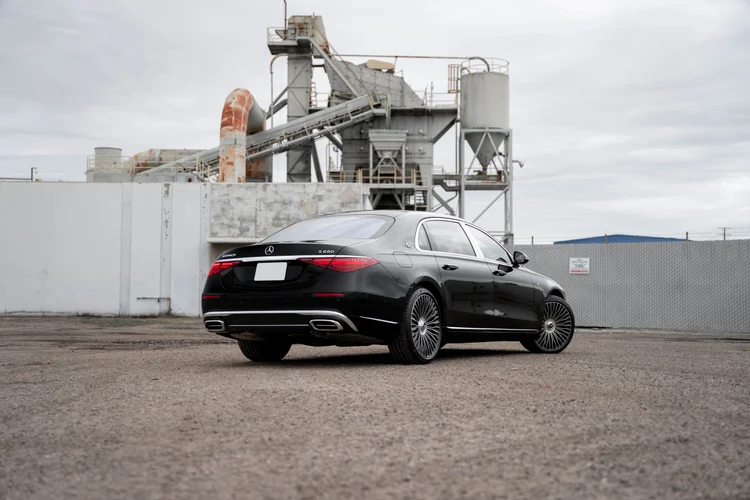 Complete rear-three-quarter view of the black Mercedes-Maybach S 680 with red lamps and silver multispoke wheels below industrial structures